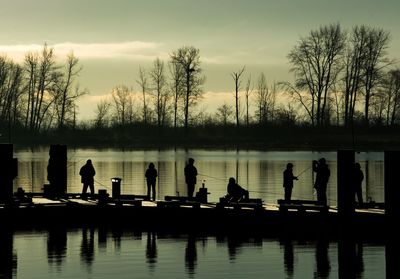 Silhouette people fishing at lake against sky during sunset