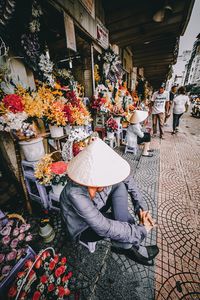 Vendor wearing asian style conical hat sitting at flower market in city