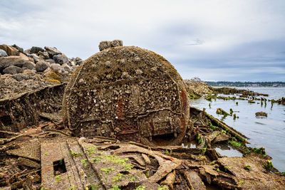 Damaged rocks on shore against sky