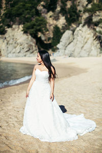 Bride standing at beach during sunny day