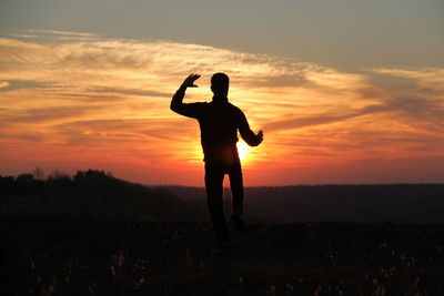 Silhouette man standing on field against sky during sunset