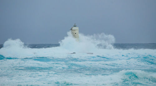 Waves splashing on shore against clear sky