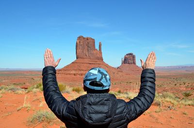 Rear view of man standing with arms raised at monument valley tribal park