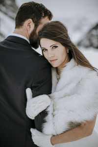 Bride in wedding dress and fur rests head against groom in winter