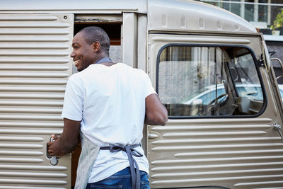 Smiling mid adult male owner opening door of food truck in city