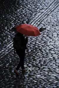 Rear view of woman with umbrella walking on cobblestone street during rainy season