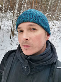 Selfie portrait of a man in clothes and a blue hat in the forest in winter