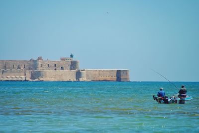 People on sea against clear blue sky