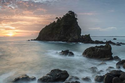 Rocks in sea against sky during sunset