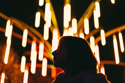 Low angle view of silhouette woman against illuminated lights at night