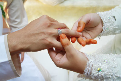 Midsection of woman putting ring on man hand during wedding