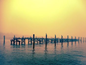 Silhouette wooden posts in sea against clear sky