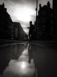 Silhouette people on wet road against sky