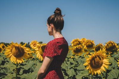 Low angle view of woman standing on sunflower field against clear sky