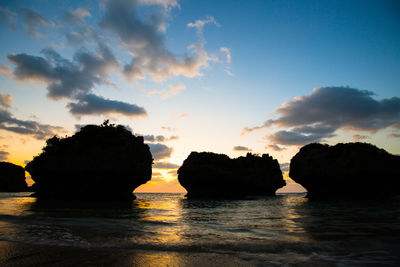 Silhouette rocks on sea against sky during sunset