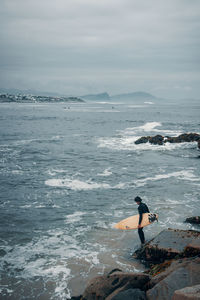 Young man surfing in sea against cloudy sky