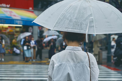 Rear view of woman with umbrella walking on street during rainy season