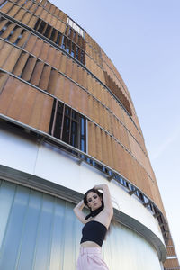Confident young woman in a modern suit stands by a wall of a modern building and looks at the camera