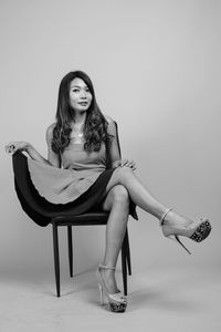 Portrait of woman sitting on chair against gray background