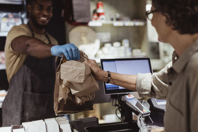 Male owner giving package order to female customer in delicatessen shop