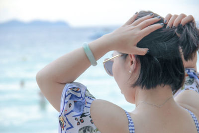 Woman tying hair at beach during sunset