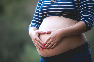 Midsection of pregnant woman making heart shape on abdomen