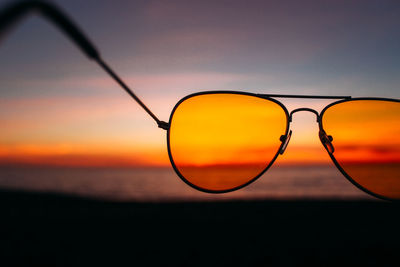 Close-up of sunglasses against sky during sunset