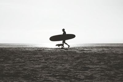 Silhouette of surfer and dog walking on beach