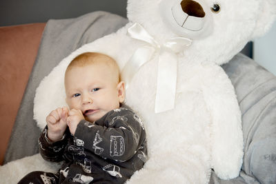 Smiling newborn baby and big white teddy bear sitting on sofa or couch