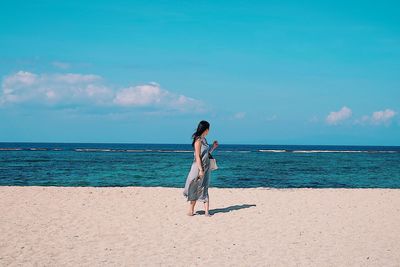 Rear view of woman standing on beach against sky