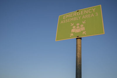 Low angle view of road sign against clear blue sky