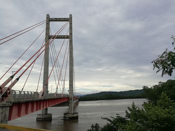 View of suspension bridge over river against cloudy sky