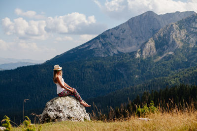 Full length of woman relaxing on rock against mountain