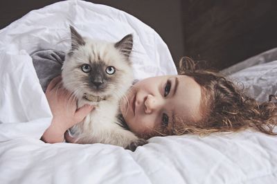 Cute girl lying with cat on bed