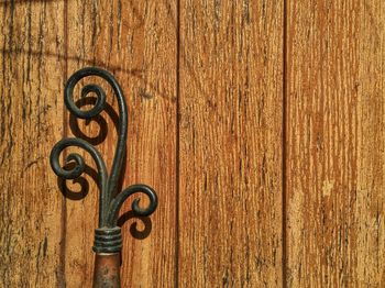 Close-up of wrought iron against wooden wall during sunny day