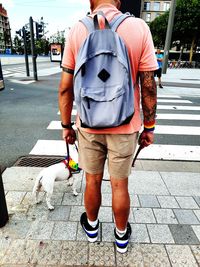 Rear view of man with dog standing on footpath