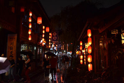 People walking on illuminated street amidst buildings at night