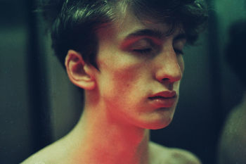 Close-up of shirtless young man with eyes closed standing in darkroom