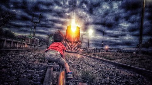 Rear view of man on railroad tracks against sky during sunset
