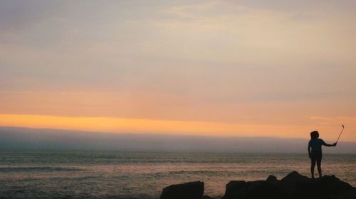 Silhouette man standing on beach against sky during sunset