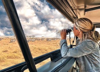 Woman photographing against sky seen through car window