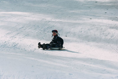 Cute boy sledding on snow covered field during winter