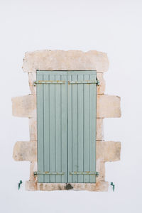 Old window with wooden light green painted closed shutters on white wall