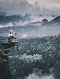 Rear view of hiker sitting on cliff during foggy weather