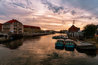 Boats moored on canal by buildings against sky during sunset