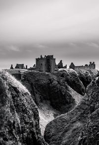 Low angle view of old ruin on rock formation against cloudy sky