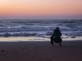 Rear view of man on beach against sky during sunset