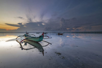 Fishing boat on beach against sky during sunset
