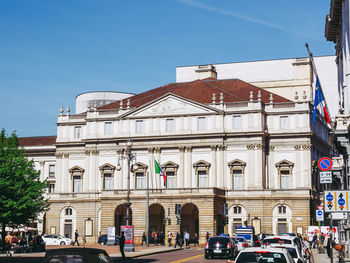 Cars on road by buildings against blue sky