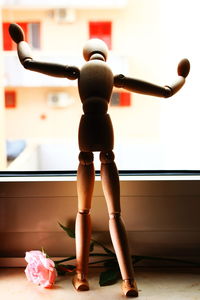 Close-up of wooden figurine by rose on window sill at home